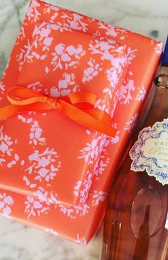 an orange gift box sitting next to a bottle of wine and a lace doily