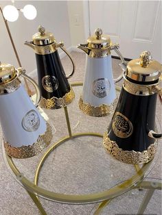 four coffee pots sitting on top of a round glass table with gold trimmings