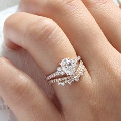 a woman's hand with two wedding rings on her finger and the ring has an oval shaped diamond surrounded by smaller round diamonds