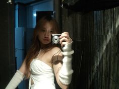 a woman taking a selfie with her camera in a bathroom mirror while wearing white gloves