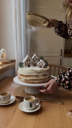 a woman is pouring frosting onto a cake on a table with cups and saucers