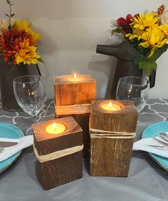 four wooden blocks with lit candles sitting on top of a table next to plates and glasses