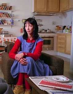 a woman sitting in a living room next to a table with books on top of it