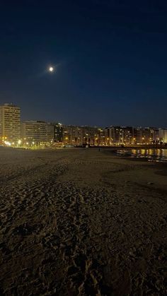 the moon shines brightly in the night sky over a beach and cityscape