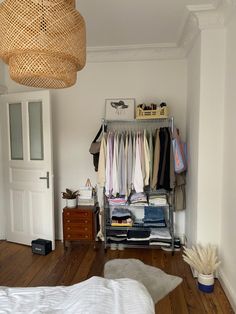 a closet with clothes hanging from it's ceiling and a bed in the foreground