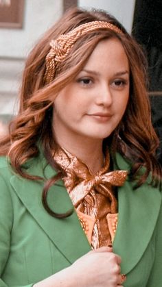 a woman wearing a green coat and gold tie with her hair in the wind,