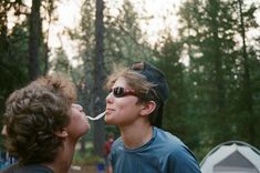 two young boys are blowing bubbles out of their mouths in front of tents and trees