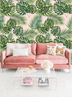 a pink couch sitting in front of a wall with green palm leaves on the wall