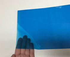 a hand is holding up a blue piece of paper on a white surface, with the edge of it folded in half