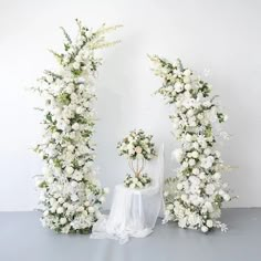 two white flowers are arranged in the shape of an arch and table with a cloth draped over it