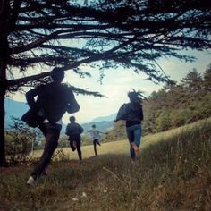 four people are running in the grass near some trees