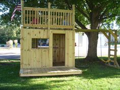 a small wooden play house with a flag on the roof and a tree in the yard