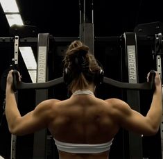 a woman with headphones on working out in the gym while looking at her back