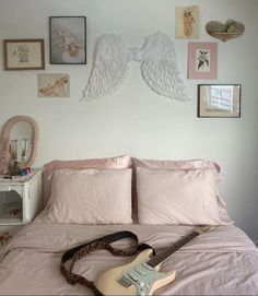 a guitar laying on top of a bed with pink sheets and pictures hanging above it