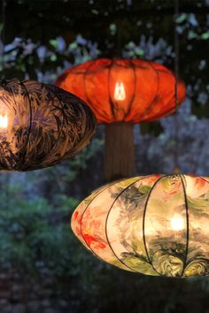 three different colored lamps hanging from the ceiling in front of trees and bushes at night