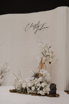 a table topped with white flowers and plants next to a wall that says congratulations on it