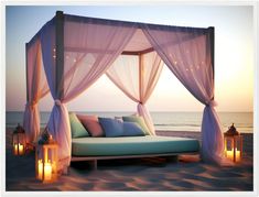 an outdoor bed on the beach with lanterns lit up at night and in front of it