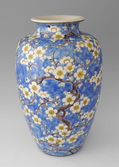 a blue vase with white and yellow flowers painted on the side, sitting against a gray background