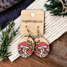 the earrings are made from wood and have red mushrooms on them, with words sugarnspicc printed on them