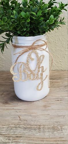 a white mason jar filled with greenery on top of a wooden table