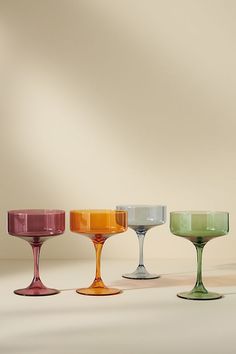 four different colored wine goblets lined up in a row on a white surface