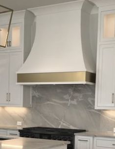 a kitchen with marble counter tops and white cabinets, along with an oven hood over the range