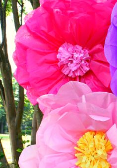 three large pink and purple paper flowers in front of trees