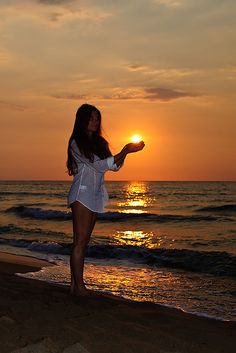 a woman is standing on the beach at sunset