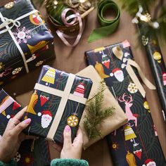 a person holding wrapped presents on top of a table next to christmas decorations and wrapping paper