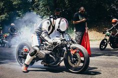 a man riding on the back of a motorcycle down a street next to other people