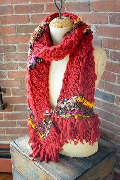 a mannequin wearing a red scarf on top of a wooden table next to a brick wall