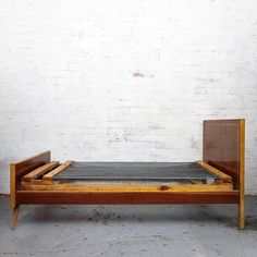 a wooden bed frame sitting in front of a white brick wall with no sheets on it