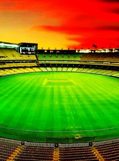 an empty soccer stadium with the sun setting in the background and green grass on the field