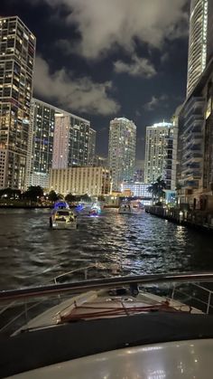 a boat traveling down a river in front of tall buildings at night with lights reflecting off the water