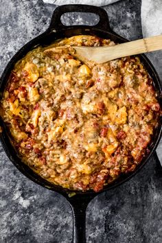 a skillet filled with food on top of a table next to a wooden spoon