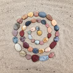 several rocks arranged in the shape of a spiral on top of sand, with one circle made out of them