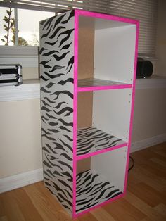 a cardboard box with zebra print and pink trim on the bottom shelf in front of a window