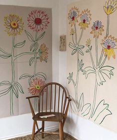 a wooden chair sitting in front of a wall with flowers painted on it