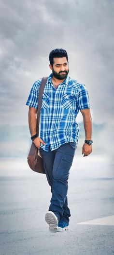 a man with a beard and blue shirt is walking on the beach while carrying a brown bag