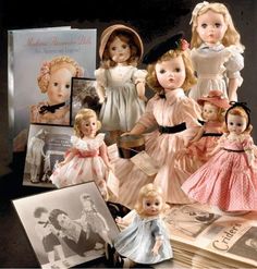 an assortment of dolls and books on a table with pictures, cards, and other items