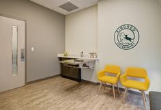 two yellow chairs sitting in front of a white wall with a green logo on it