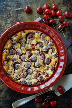 a cherry cobbler in a red bowl with fresh cherries around it