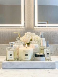 a bathroom counter with candles, soaps and flowers on it in front of two mirrors