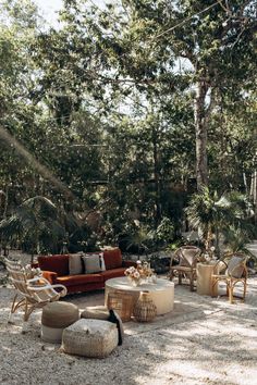 an outdoor seating area with wicker furniture and large trees in the background, surrounded by gravel