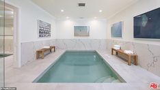 an indoor swimming pool with marble walls and flooring in the middle, along with two wooden benches on either side