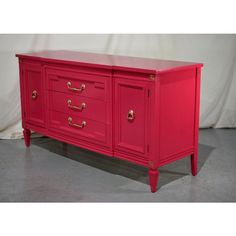 a red dresser with gold handles and drawers on it's sides, in front of a white backdrop