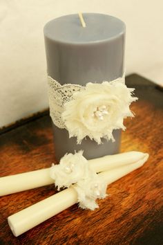 two candles with lace and flowers on them sitting on a table next to a candle holder