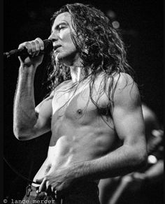 a shirtless man with long hair holding a microphone