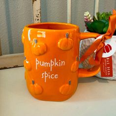 an orange mug sitting on top of a white table next to a potted plant