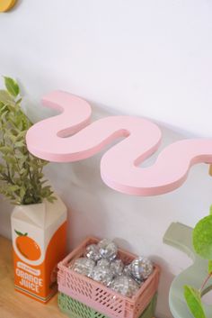 a pink wooden sign sitting on the side of a wall next to some plants and boxes